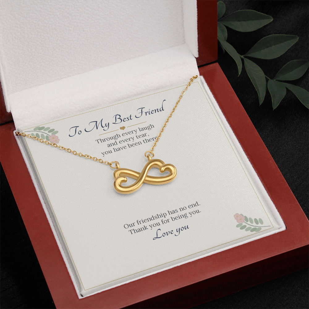 Yellow gold finish infinity heart necklace on the To My Best Friend card in an open wooden luxury box, seen from above with leaves beside it