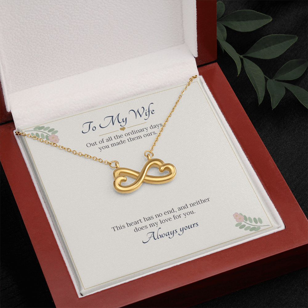 Yellow gold finish infinity heart necklace on the To My Wife card in an open wooden luxury box, seen from above with leaves beside it