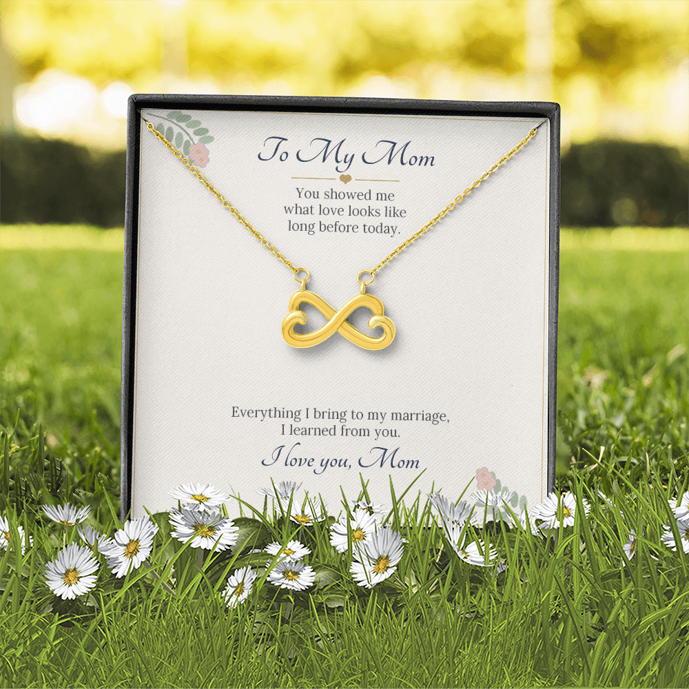 Yellow gold finish infinity heart necklace on the To My Mom wedding card in a gift box on the grass with daisies